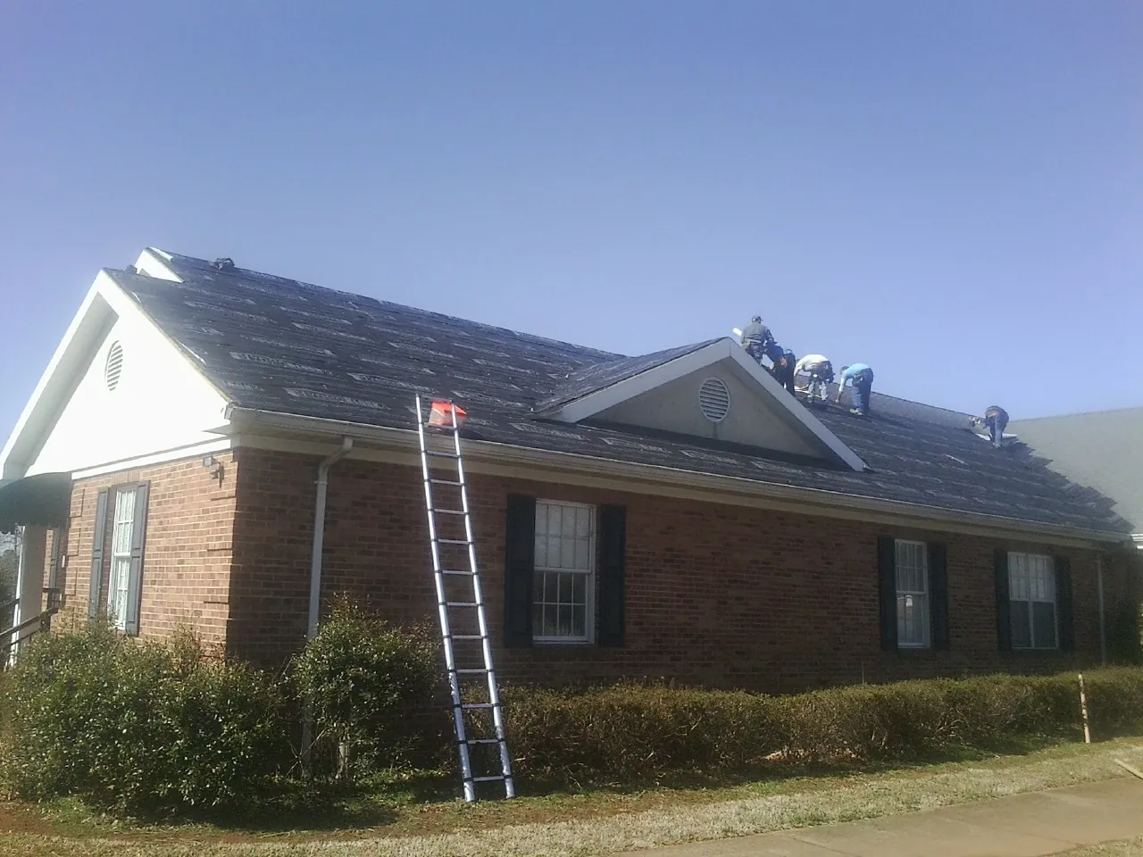 Crew tearing shingles off a brick ranch roof with a ladder set — Metal Roof Repair work by our crew in Hamshire