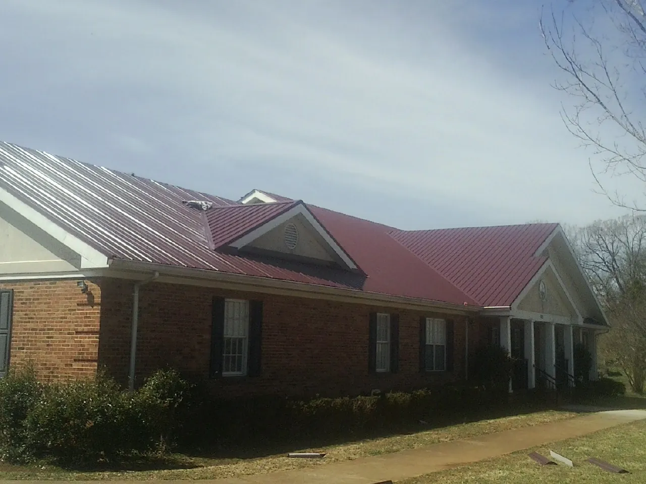 Red metal roof with gabled entries on a long brick building, from a Hail Damage Roof Repair job in Hamshire