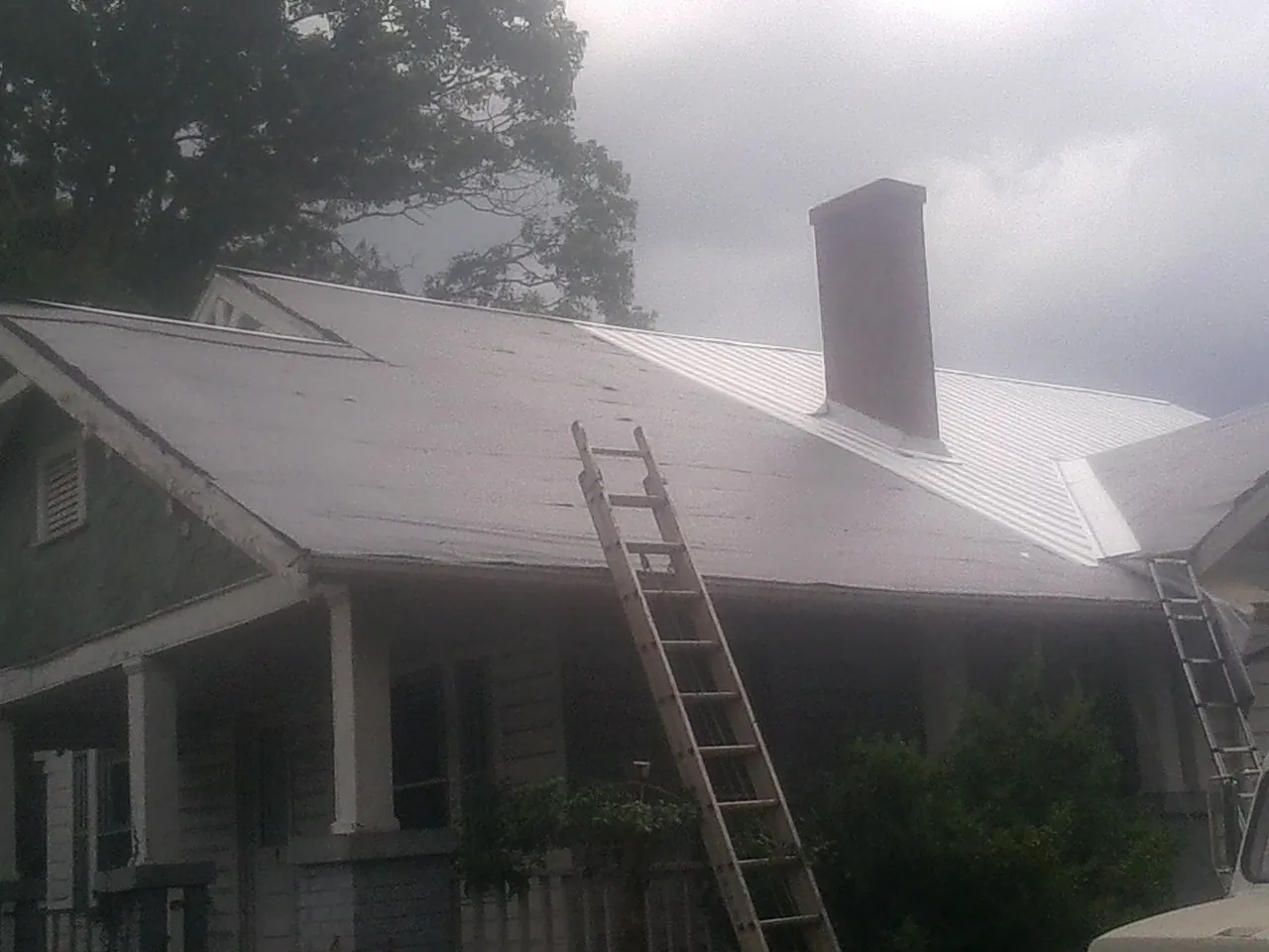 Ladders against a metal roof on an older home with a brick chimney in Hamshire
