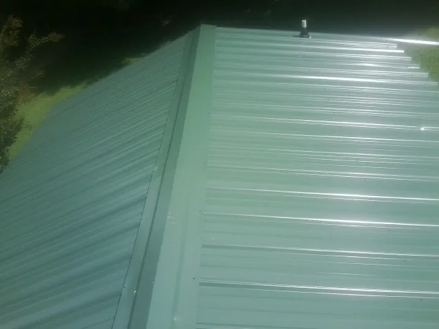 New green metal panels meeting at the ridge of a roof — Flat Roof Repair work by our crew in Hamshire