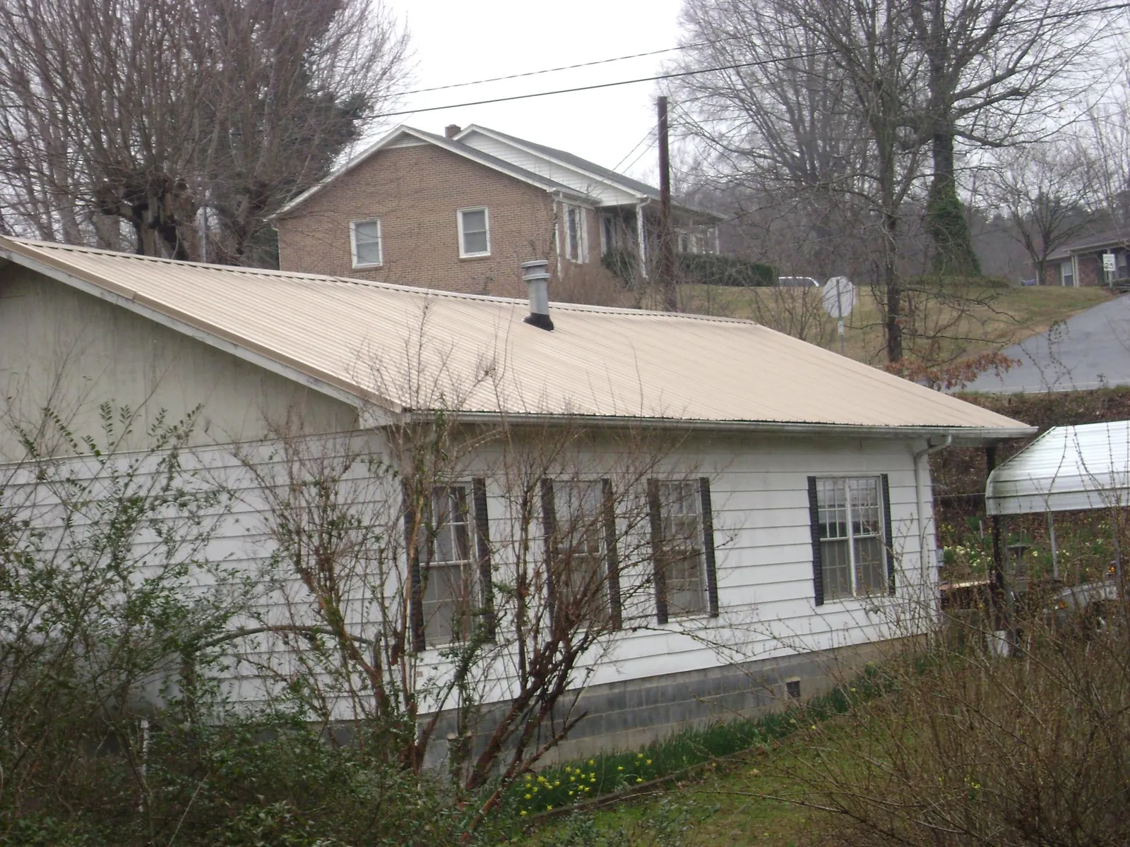 Tan metal roof on a white sided house set into a hillside — Commercial Roofing by Roofing Brothers in Hamshire